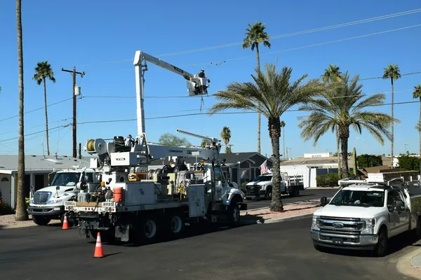 Utility bucket truck working on overhead lines on a street lined with palms