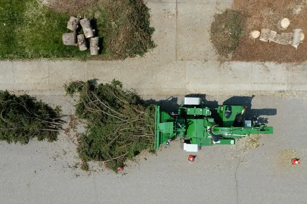 Overhead view of a chipper on a street beside cut branches and trunk rounds