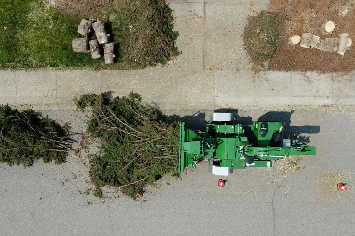 Overhead view of a chipper on a street beside cut branches and trunk rounds